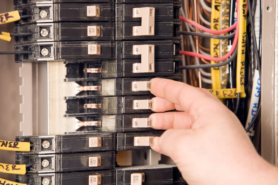 Electrician toggling a switch on an open residential electrical breaker panel.
